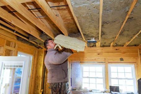 Worker installs insulation material in a wooden house during construction on a winter day.